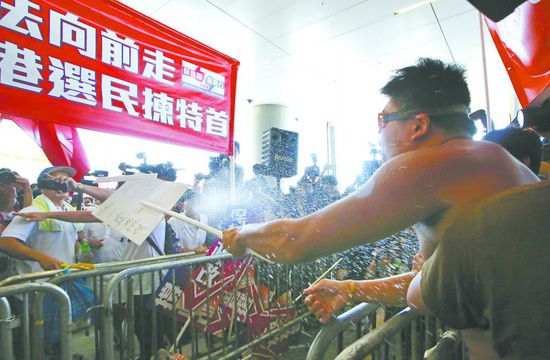 17日，在香港立法會外，一名反對政改的男子向支持派人群投擲標牌。