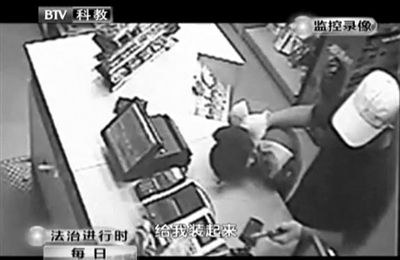 戴帽男子一手掐住加油站營(yíng)業(yè)員，一手持發(fā)令槍指向另一營(yíng)業(yè)員，要求“把錢給我裝起來”。