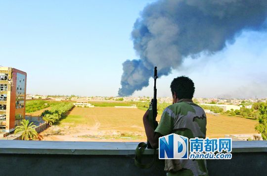 2日，利比亞首都的黎波里，一民兵武裝成員眺望被火箭彈擊中的儲(chǔ)油罐冒出濃煙。