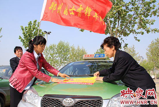　　授旗結(jié)束后，首都的士雷鋒車隊王鳳進隊長（右）與鄭州的的哥的姐在車身上貼上標(biāo)識。