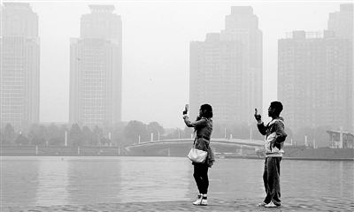 29日中午，鄭東新區(qū)如意湖畔，兩個(gè)年輕人拍攝霧霾中的景色。 鄭州晚報(bào)記者 馬健 圖