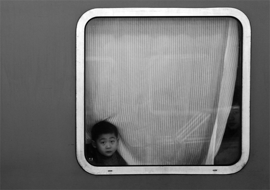 一個孩子把頭伸向窗外，他想再看送別的親人一眼