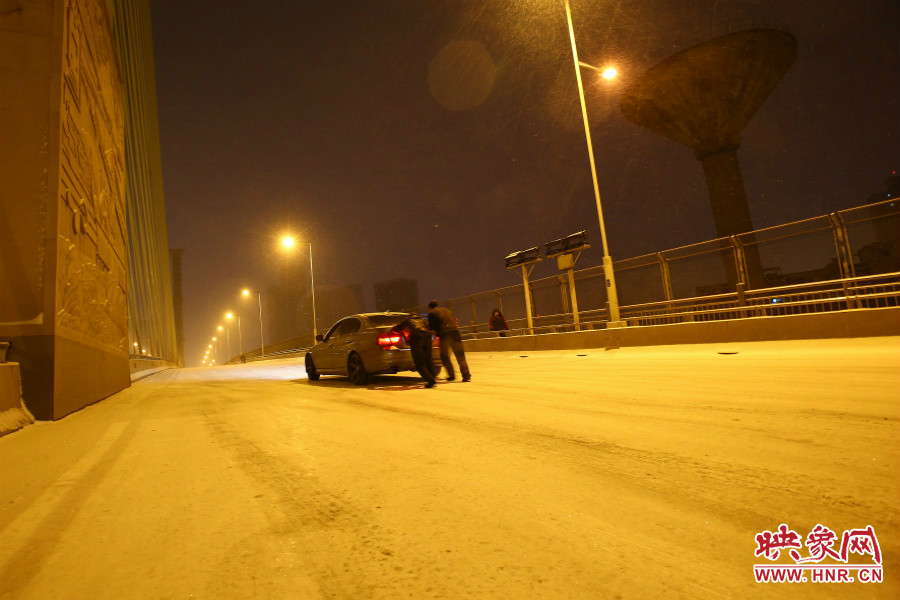 雪天路滑，汽車上橋打滑，兩名“推車人”幫助一輛私家車上坡。