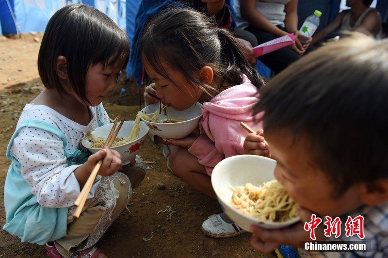 2014年8月6日，云南魯?shù)辇堫^山災(zāi)區(qū)，兒童在帳篷外吃飯。