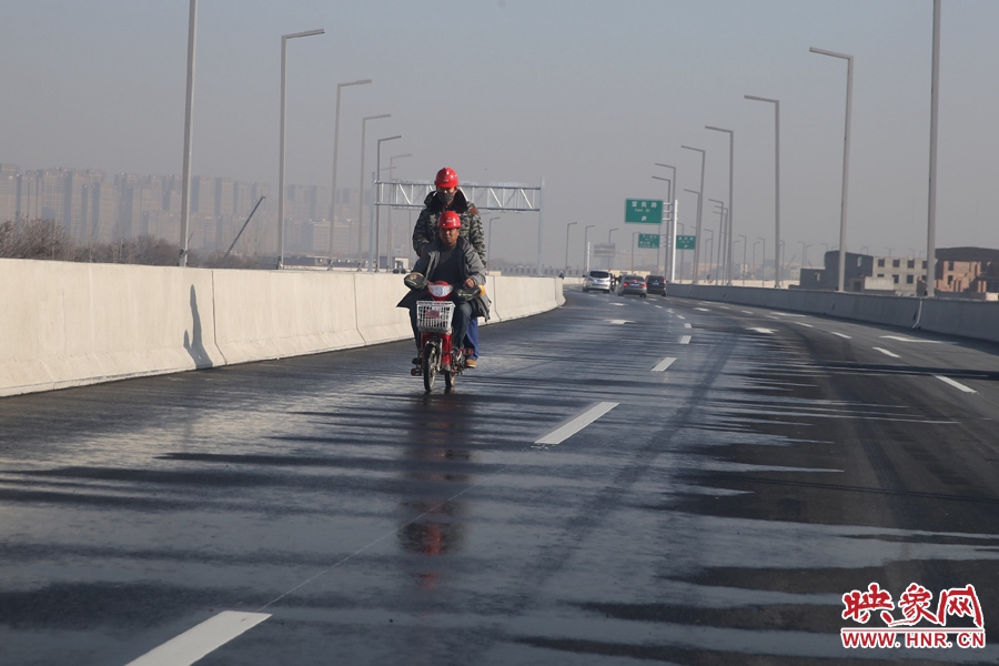 兩名工人騎車經(jīng)過(guò)灑水養(yǎng)護(hù)路面。
