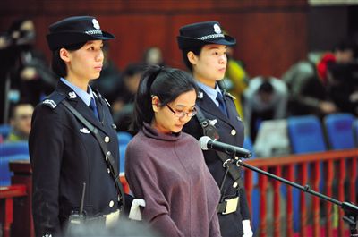 被告人盧梅低著頭，站在朝陽(yáng)法院刑事審判庭的被告席上。